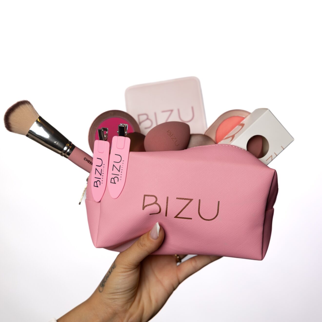 Pink makeup bag with BIZU branding containing makeup items on a white background