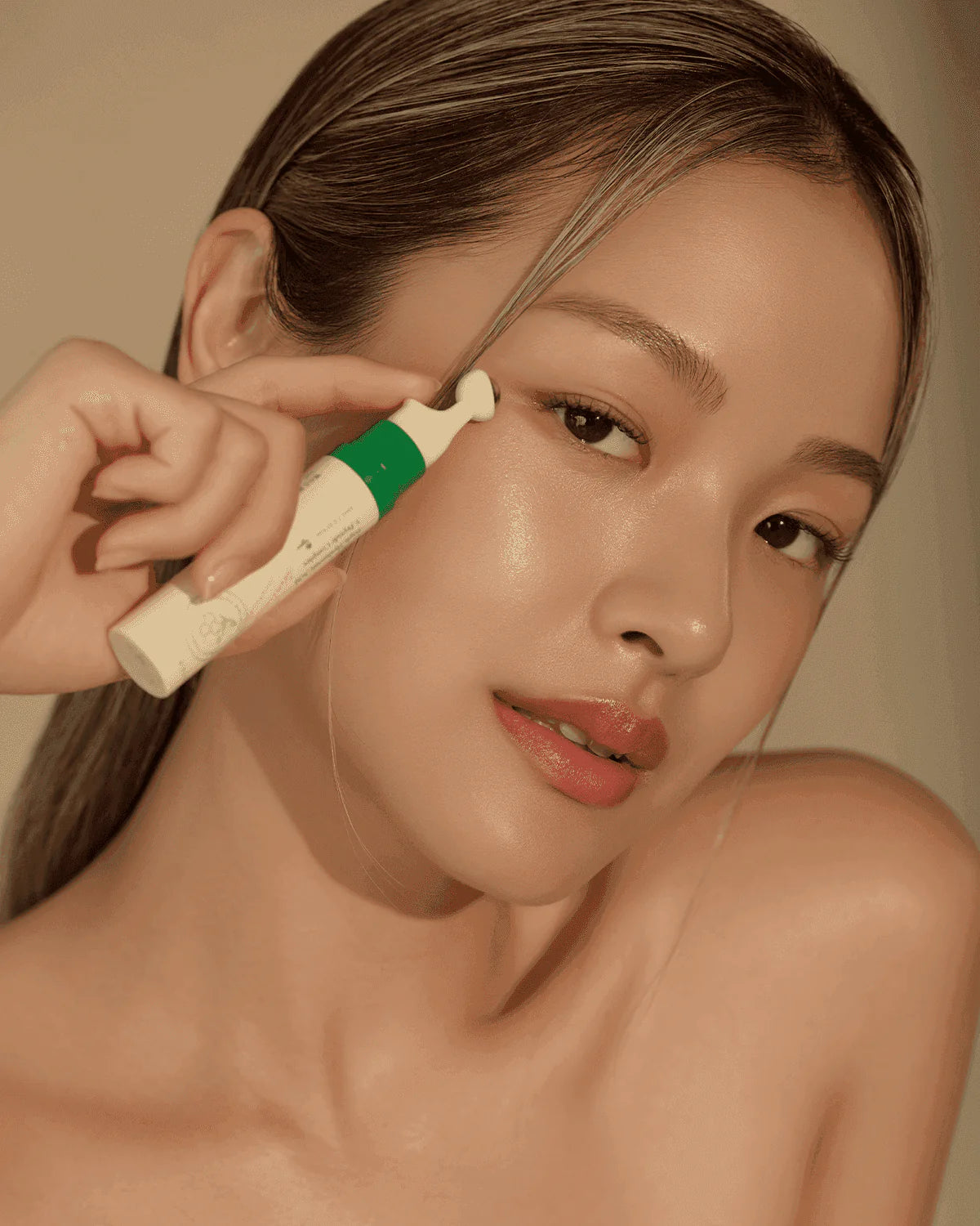 Woman using an Axis-Y Vegan Collagen Eye Serum skincare tool on her face with a neutral background